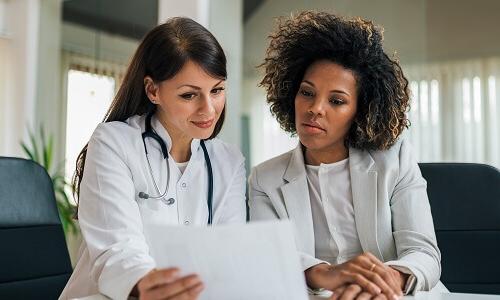 Healthcare administrator collaborating with a doctor in an office setting, reviewing documents to align on patient care strategies.
